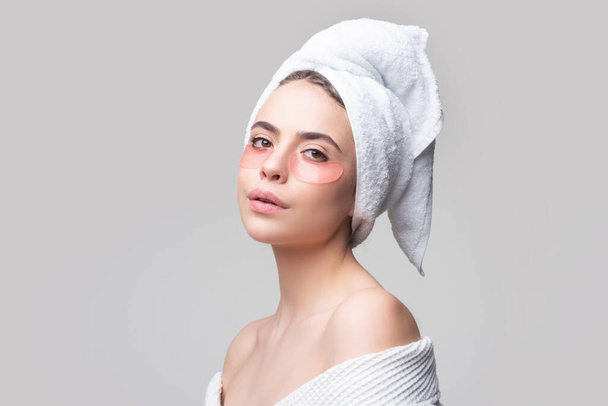 Woman applying eye patches. Close up portrait girl with towel on head. Portrait of beauty woman with eye patches showing an effect of perfect skin. Brunette spa girl applying anti-fatigue mask. - Foto, Imagem