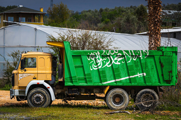 サウジアラビアの国旗をイメージしたダンプトラックは、田舎の背景に駐車されています。輸出入、輸送、商品の国内配送の概念 - 写真・画像