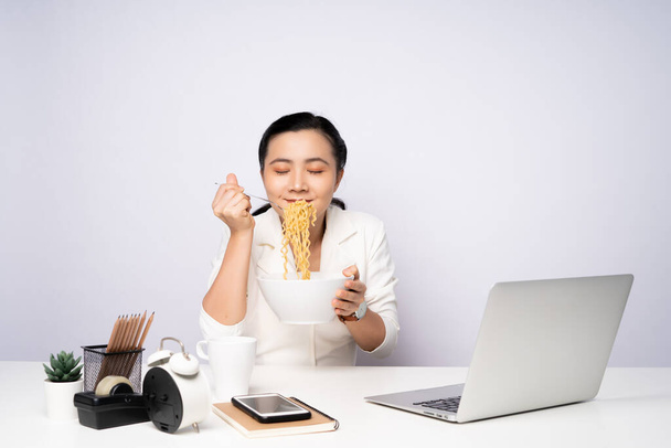 Азиатка ест лапшу после работы сверхурочно. Бизнесмен довольна лапшой после окончания работы. - Фото, изображение
