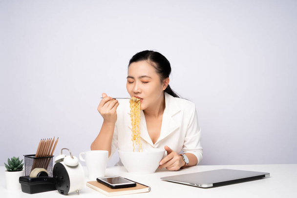 Azjatka jedząca makaron po nadgodzinach w biurze. Bizneswoman szczęśliwy z makaronem po zakończeniu pracy. - Zdjęcie, obraz