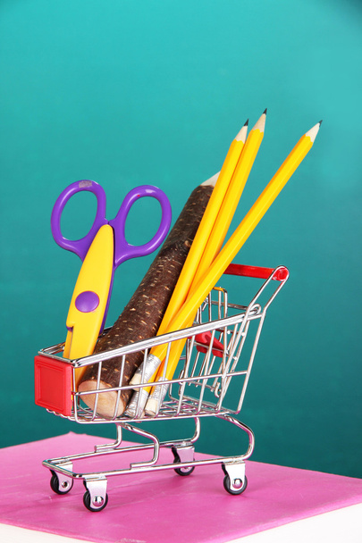 School supplies in supermarket cart on blackboard background - Foto, Bild