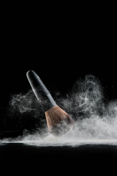 Κοντινό πλάνο σε σκόνη και πινέλο για makeup artist ή blogger ομορφιάς σε μαύρο φόντο - Φωτογραφία, εικόνα
