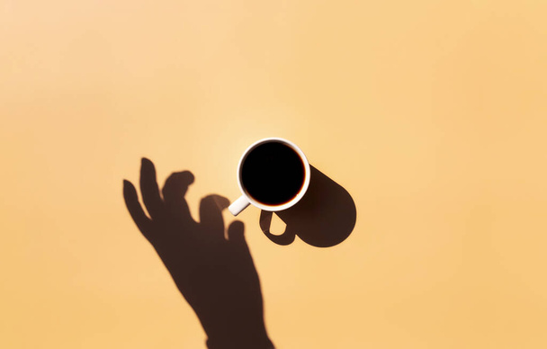 Šálek kávy a talíř, slunce a ruční stín na žluté béžové terakotové pozadí - Fotografie, Obrázek
