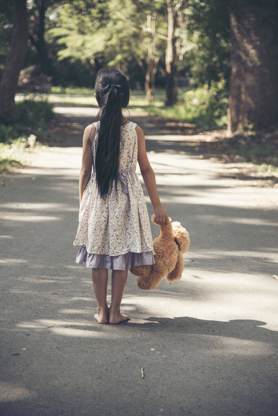 Sad girl hugging teddy bear sadness alone in green garden park. Lonely girl feeling sad unhappy walking outdoors with best friend toy. Autism child play teddy bear best friend. Family violence concept - Photo, Image