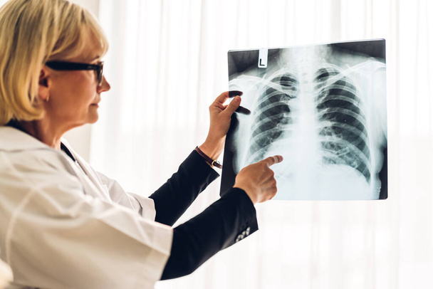 Attractive senior woman doctor wearing uniform with stethoscope looking at chest x-ray film photo of patient with lung pneumonia.healthcare and medicine - Foto, Imagen