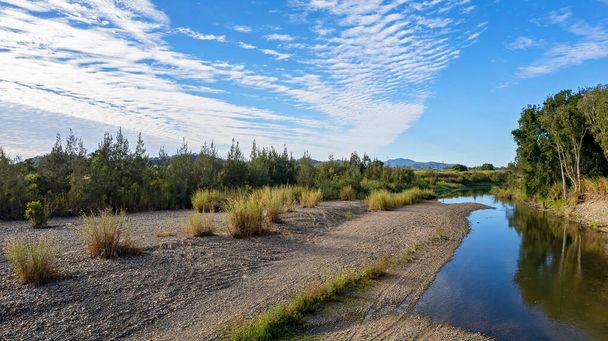Ecosistema acuático de un arroyo rural bajo un cielo azul nublado - Foto, Imagen