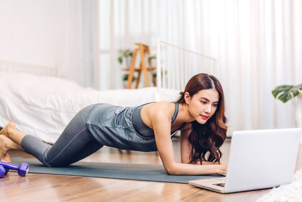 Portrait of sport asian woman in sportswear sitting relax and practicing yoga and do fitness exercise with laptop computer in bedroom at home.Diet concept.Fitness and healthy lifestyle - Фото, изображение