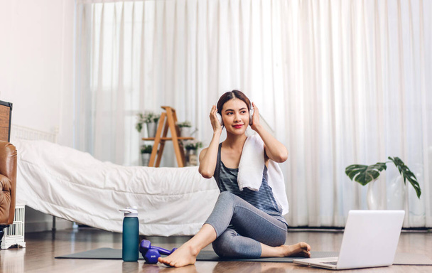 Portrait of sport asian woman in sportswear sitting relax and practicing yoga and do fitness exercise with laptop computer in bedroom at home.Diet concept.Fitness and healthy lifestyle - Photo, Image