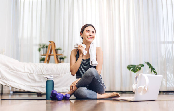 Portrait de sport asiatique beauté corps mince femme en vêtements de sport assis se détendre et pratiquer le yoga et faire des exercices de remise en forme avec ordinateur portable dans la chambre à coucher à la maison. - Photo, image