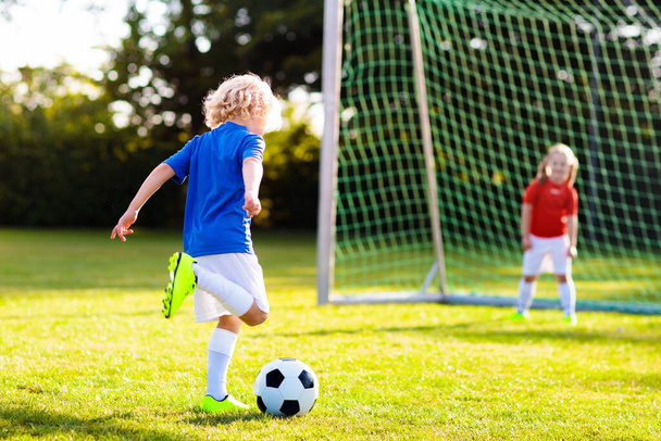 Kids play football on outdoor field. Children score a goal during soccer game. Little boy kicking ball. Running child in team jersey and cleats. School football club. Sports training for young player. - Foto, Imagem