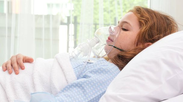 Cute little asian girl with oxygen pipe and using oxygen mask for inhalations and treatment on her face on bed in the hospital.health care,support concept - Foto, Bild