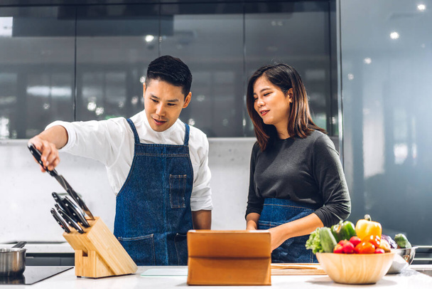Молодая азиатская семейная пара весело готовить вместе со свежим овощным салатом на table.Happy пара ищет рецепт в Интернете с планшетным компьютером, чтобы подготовить вкусный обед на кухне - Фото, изображение
