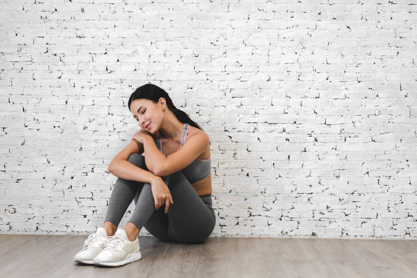 Sport woman in sportswear relax sit after workout against copy space for adding text with white wall background.Diet concept.Fitness and healthy lifestyle - Photo, Image