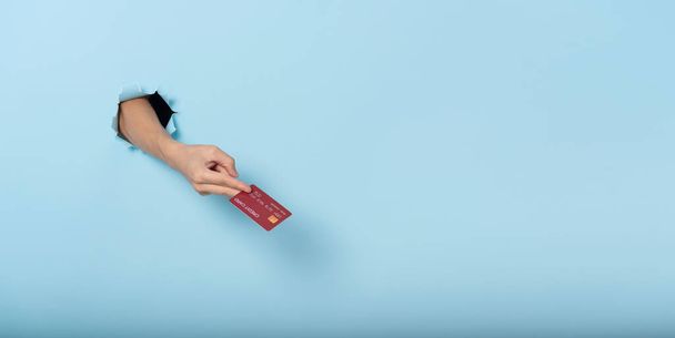 Mano de mujer sosteniendo tarjeta de crédito sobre fondo azul banner. Imagen panorámica - Foto, imagen