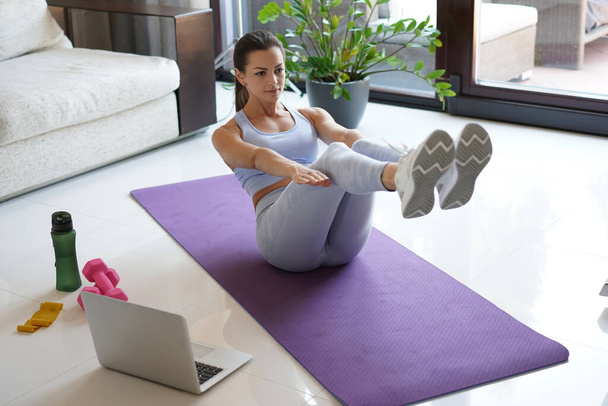 Attractive slim girl in sportswear is doing abs exercise on the floor at home. Healthy lifestyle. - Fotografie, Obrázek