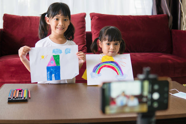 Dwóch azjatyckich dzieci uczą się online z nauczycielem przez połączenie wideo razem. Rodzeństwo uczy się w domu z laptopem komputerowym podczas kwarantanny z powodu pandemii Covida 19. - Zdjęcie, obraz