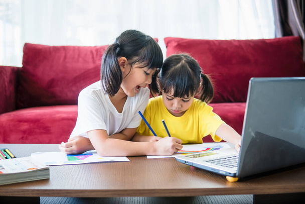 Dos niños asiáticos estudiantes estudian en línea con el maestro por videollamada juntos. Los hermanos están estudiando en casa con computadora portátil durante la cuarentena debido a la pandemia de Covid 19. - Foto, Imagen