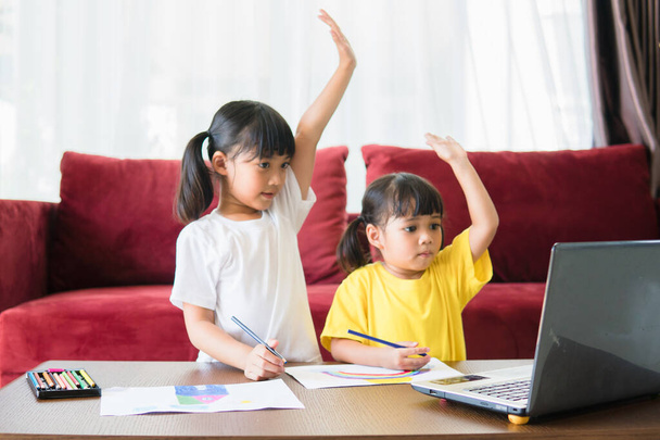 Dois asiático criança menina estudantes estudar online com professor por chamada de vídeo juntos. Os irmãos estudam em casa com computador portátil durante a quarentena devido à pandemia de Covid 19.. - Foto, Imagem