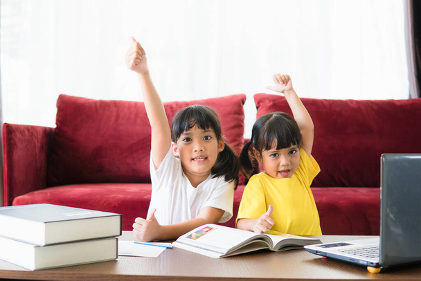 Twee Aziatische kind meisje studenten studeren online met leraar door middel van video gesprek samen. Broers en zussen geven thuis les met computer laptop tijdens quarantaine als gevolg van Covid 19 pandemie. - Foto, afbeelding