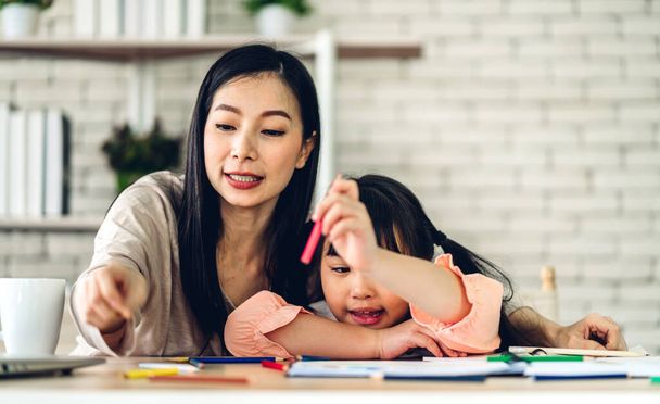 Portrait love asian family mother and little asian girl learning and writing in book with pencil making homework at home - 写真・画像