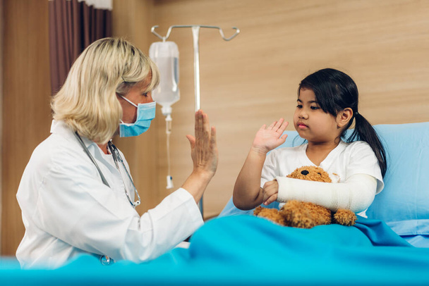 Naislääkäri yllään suojaava naamio palvelu auttaa keskustelemaan ja konsultointi puhua pikkutyttö potilas ja antaa hi viisi tarkistaa tietoja sairaalassa - Valokuva, kuva