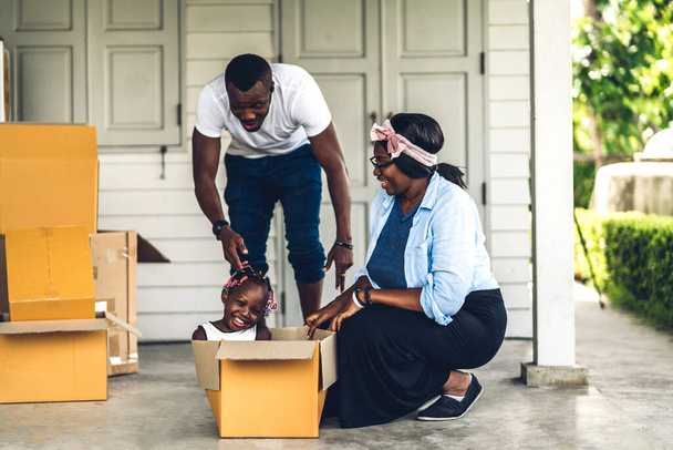 Портрет щасливої любові чорна сім'я афроамериканський батько і мати з маленькою африканською дівчинкою посміхаються сидячи в картонній коробці в новому будинку, розпаковуючись під час руху і розваги
 - Фото, зображення
