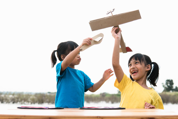Duas crianças brincando com avião de brinquedo de papelão no parque durante o dia. Conceito de jogo feliz. Criança se divertindo ao ar livre.  - Foto, Imagem