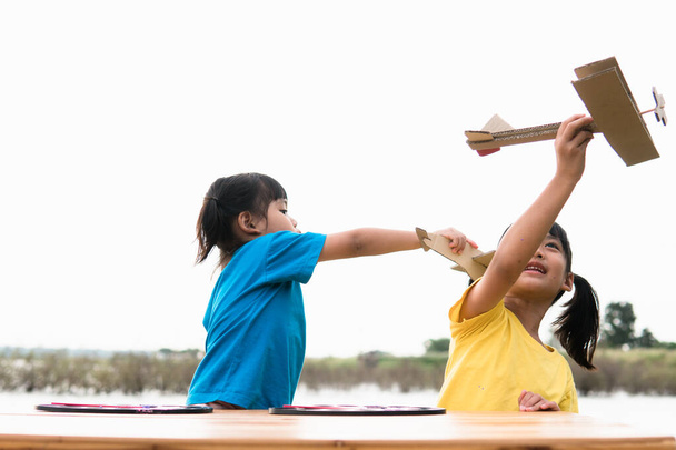 Twee kleine kinderen spelen overdag met een kartonnen speelgoedvliegtuigje in het park. Het concept van een gelukkig spel. Kind heeft plezier buiten.  - Foto, afbeelding