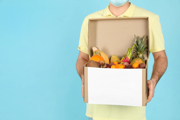 Courier holding box with assortment of exotic fruits on turquoise background, closeup. Space for text - Фото, зображення