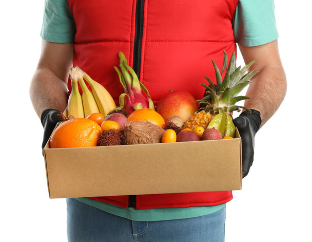 Courier holding box with assortment of exotic fruits on white background, closeup - Photo, Image