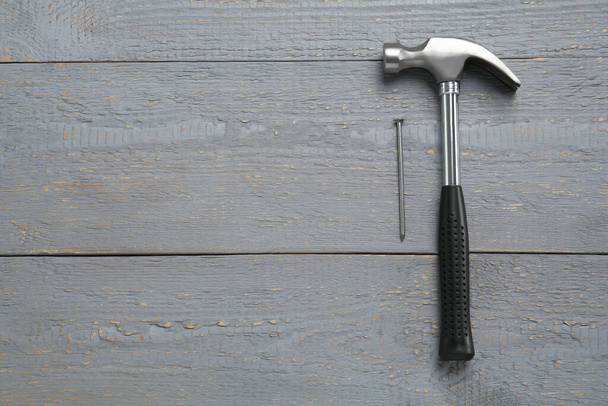 Hammer and metal nail on grey wooden table, flat lay. Space for text - 写真・画像