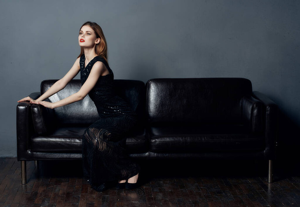 attraktive Frau im schwarzen Kleid sitzt auf dem Sofa Lächeln Kosmetik Interieur - Foto, Bild