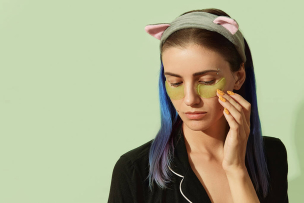 Frau im Pyjama mit Augenklappen auf pastellgrünem Hintergrund - Foto, Bild