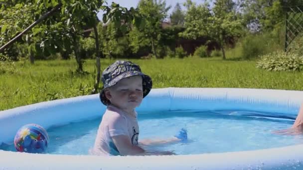 Маленький ребенок сидит в детском бассейне с водой в жаркий летний день - Кадры, видео