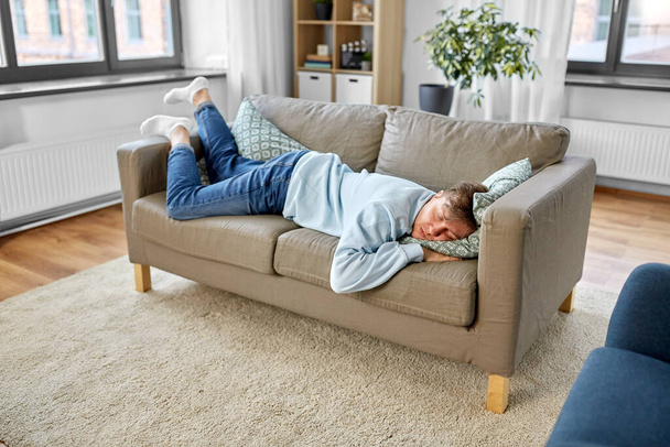 young man sleeping on sofa at home - Foto, afbeelding