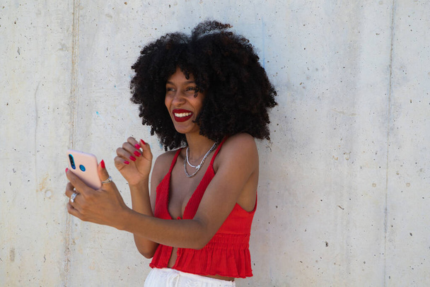 Schöne Afroamerikanerin, die per Videoanruf spricht, ist sehr glücklich. Die Frau trägt ein rotes Oberteil. Videotelefonkonzept. - Foto, Bild