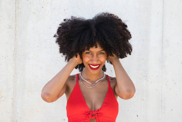 mooie afro-Amerikaanse vrouw glimlachend en kijkend naar de camera doet verschillende houdingen en gebaren met haar gezicht. De vrouw draagt een rode top en rode lippenstift. Concept geluk - Foto, afbeelding