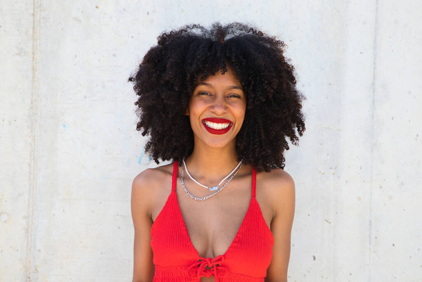 красивая афро-американская женщина улыбается и смотрит в камеру, делая различные позы и жесты с ее лицом. На женщине красный топ и красная помада. Концепция счастья - Фото, изображение