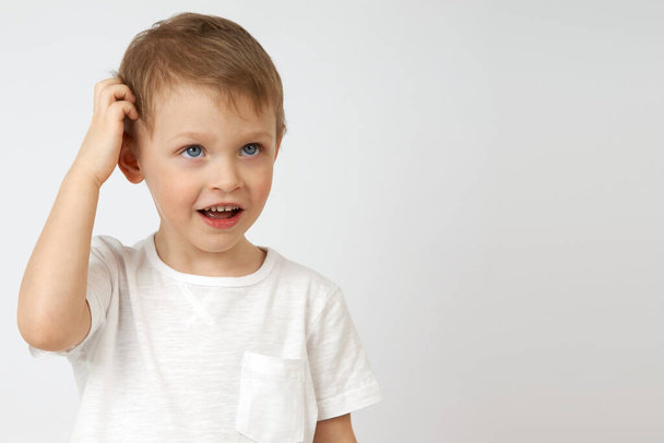 Little boy is deep in thought and scratching his head on a white background - Photo, Image