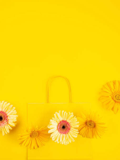 Yellow flat paper shopping bag with gerbera daisy flowers on monochrome background - Photo, Image