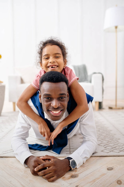 Usmívající se otec a malá dcera pózují v obýváku. Otec a žena děti volný čas v jejich domě spolu, dobrý vztah - Fotografie, Obrázek