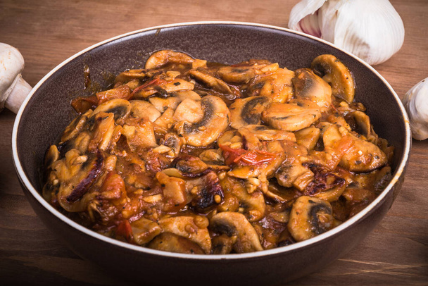 Mushroom stew in a plate. Fried mushrooms champignons with onions and tomatoes in a plate on a wooden table, close-up. - Photo, Image