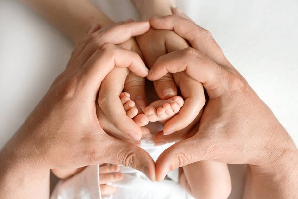Gros plan. jambes d'un nouveau-né dans les mains de maman et papa. les mains des adultes tiennent les pieds de bébé en forme de cœur. Image avec mise au point sélective - Photo, image