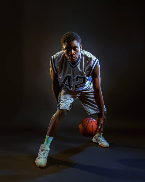 Basketball player with ball, practicing in action in studio, black background. Professional male baller in sportswear playing sport game, tall sportsman - Photo, image