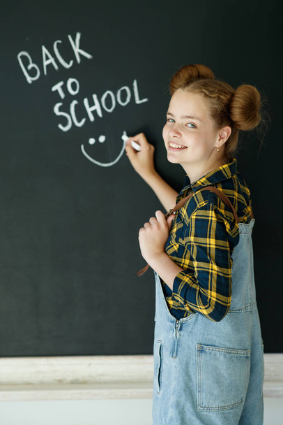 幸せな笑顔の女の子。黒板に子供。背景に黒板のある女の子の屋内教室。学校に戻ります. - 写真・画像