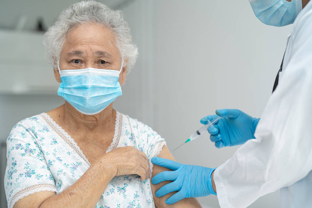 Ouderen Aziatische senior vrouw dragen gezichtsmasker krijgen covid-19 of coronavirus vaccin door arts maken injectie. - Foto, afbeelding