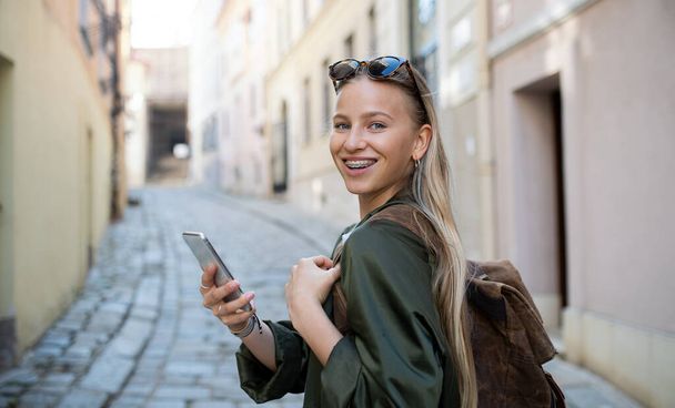 Young woman traveler in city on holiday using smartphone, looking at camera. - Foto, imagen