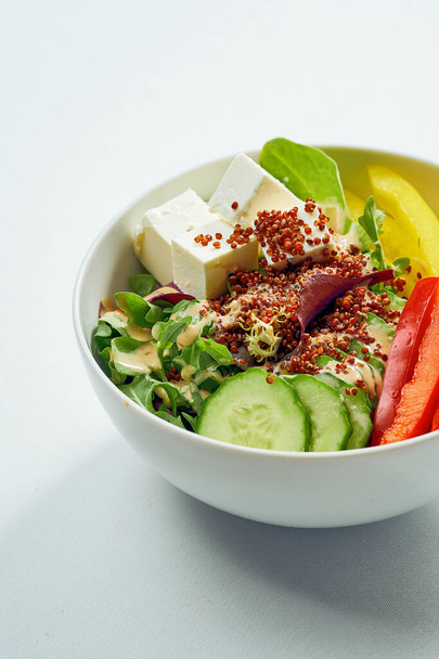 Delicious veggie bowl with cucumber, bell pepper, salad mix, quinoa and tofu in a white plate. Isolated on grey background. - Photo, image