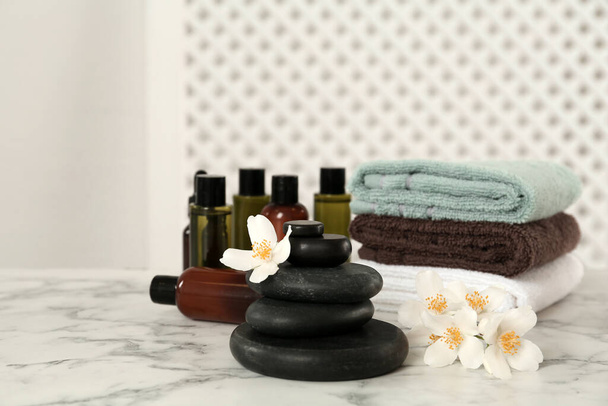 Black spa stones, beautiful jasmine flowers, towels and skin care products on white marble table - Fotografie, Obrázek