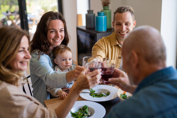 Happy multigeneration family indoors at home eating healthy lunch, clinking glasses. - Foto, Imagem